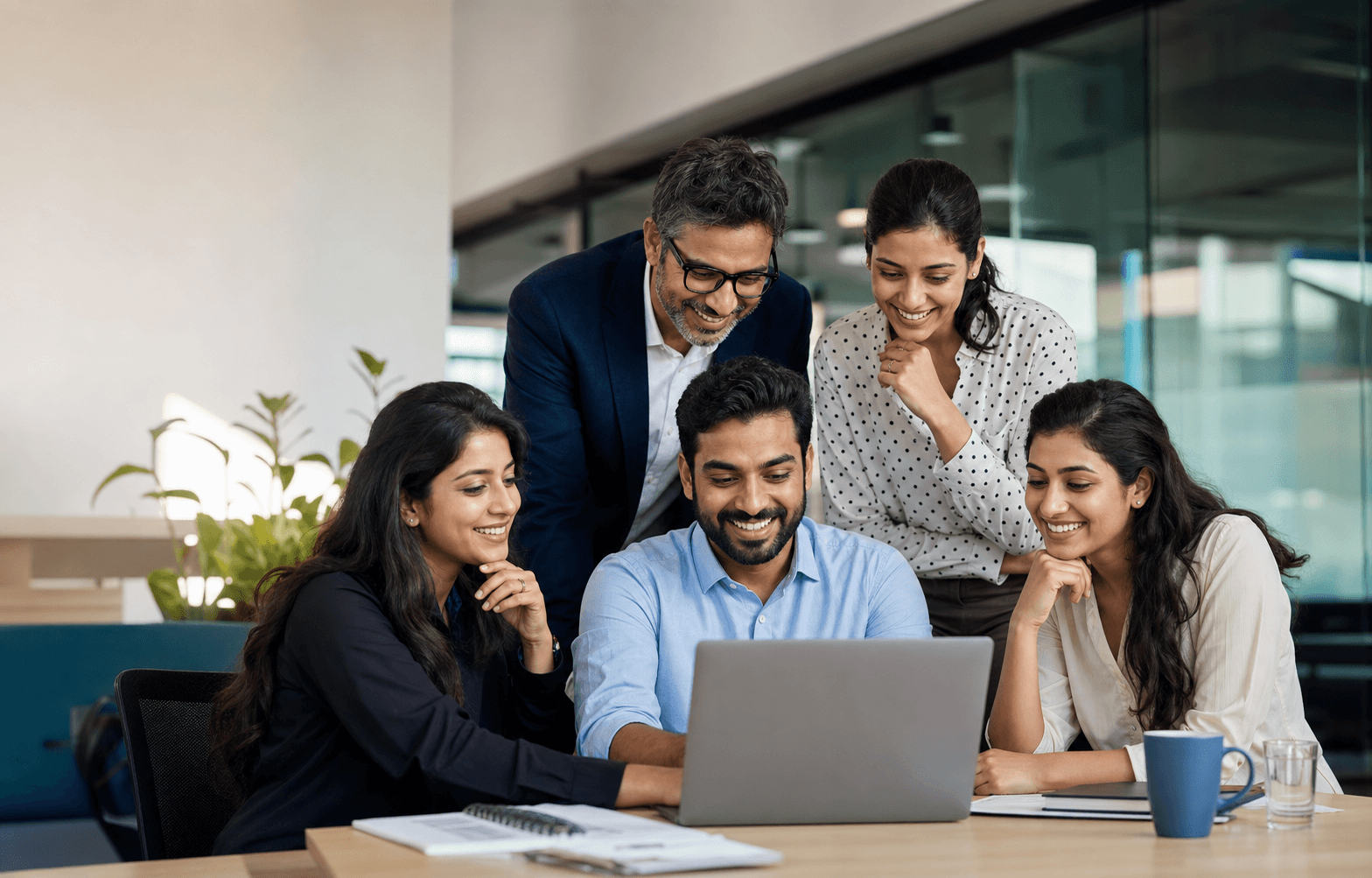 A smiling HR and finance team gathered around a laptop in a modern office